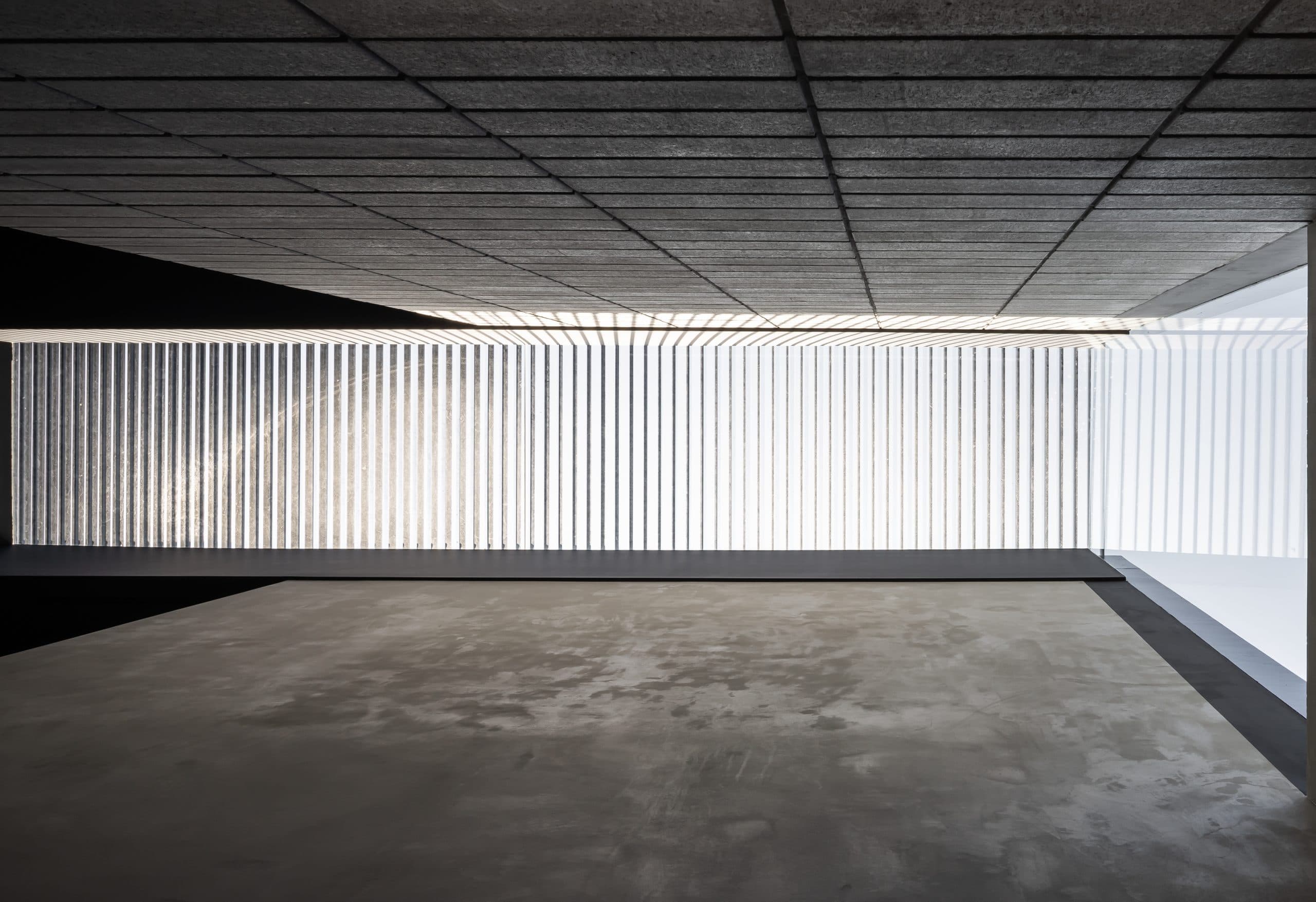 Architectural concrete interior with a ribbed ceiling, bright vertical screen, and polished concrete floor